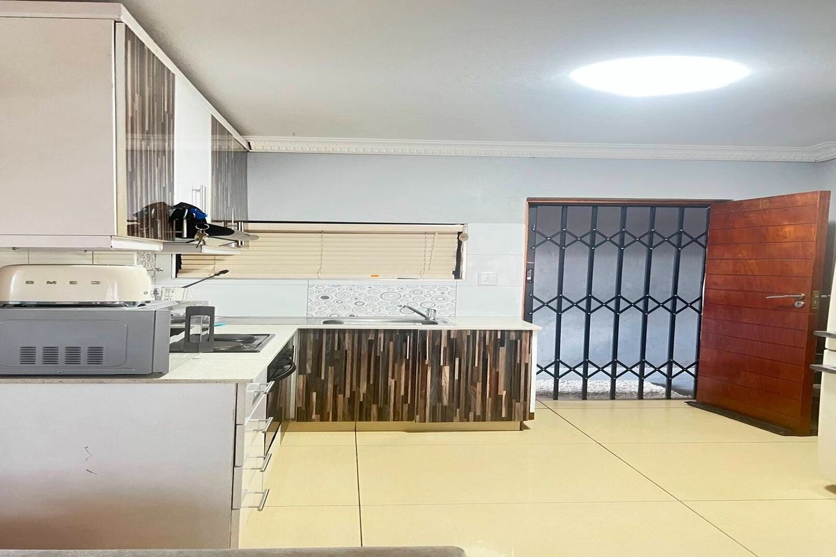 A functional kitchen featuring modern cabinetry, stone countertops, tiled flooring, and direct access to an exterior area through a secure gate and wooden door.