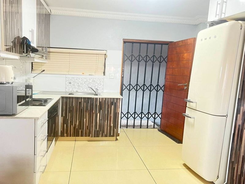 A functional kitchen featuring modern cabinetry, built-in appliances, tiled flooring, and a secure entrance door with a metal security gate.
