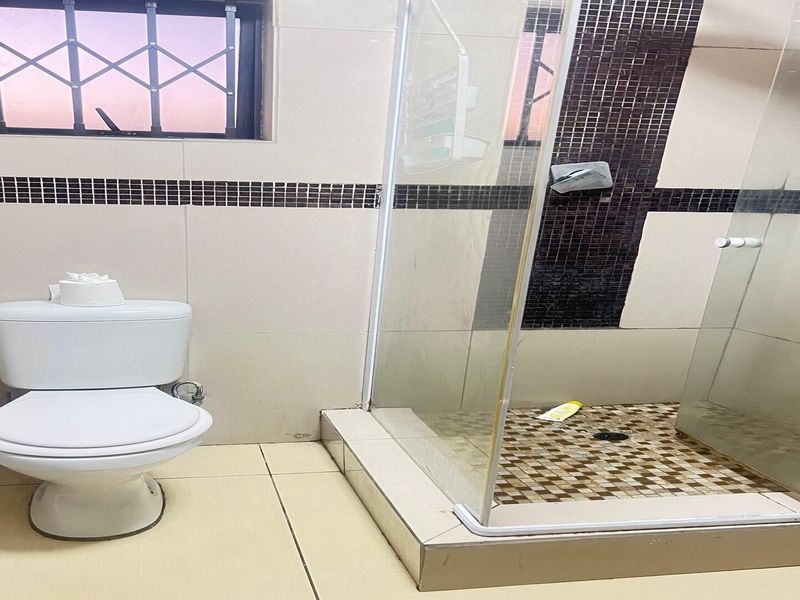 A functional bathroom featuring a glass-enclosed shower with mosaic tile accents, a standard toilet, and neutral wall tiling with a decorative border.