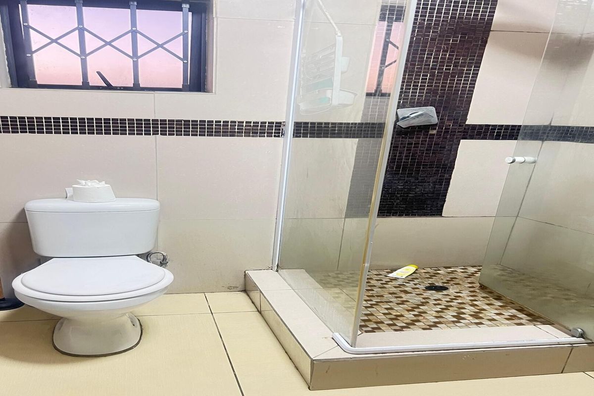A functional bathroom featuring a glass-enclosed shower with mosaic tile accents, a standard toilet, and neutral wall tiling with a decorative border.