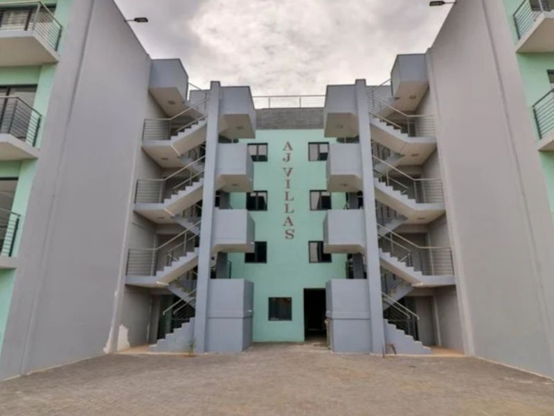 Front elevation of AJ Villas apartment complex featuring multi-level external staircases, balconies with metal railings, and a paved entrance area.