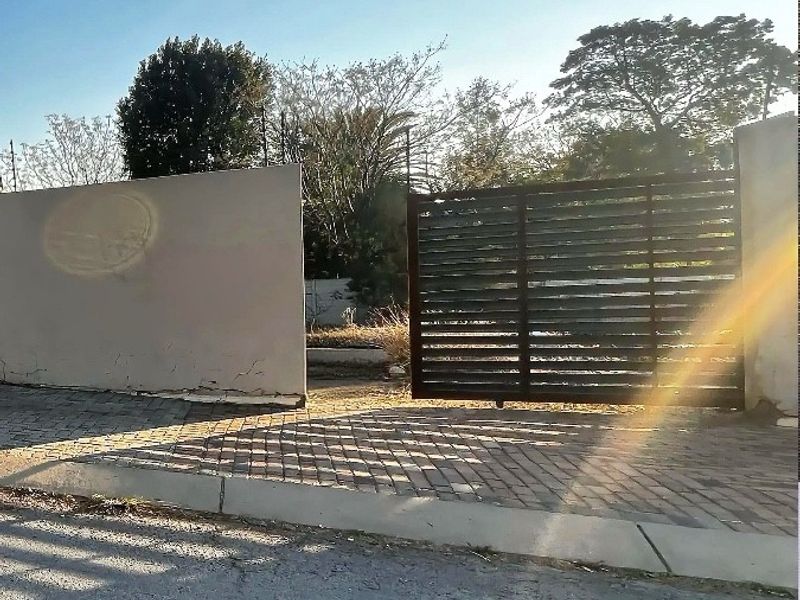 Front view of the residential property featuring a sliding gate, boundary wall, and paved driveway access from the street.