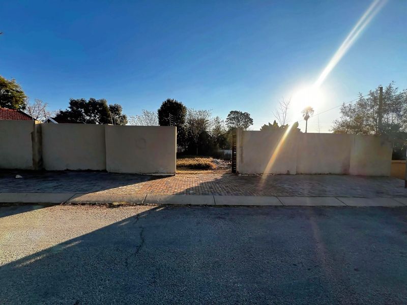 Street-level view of a vacant residential plot featuring a paved driveway entrance and perimeter boundary walls.