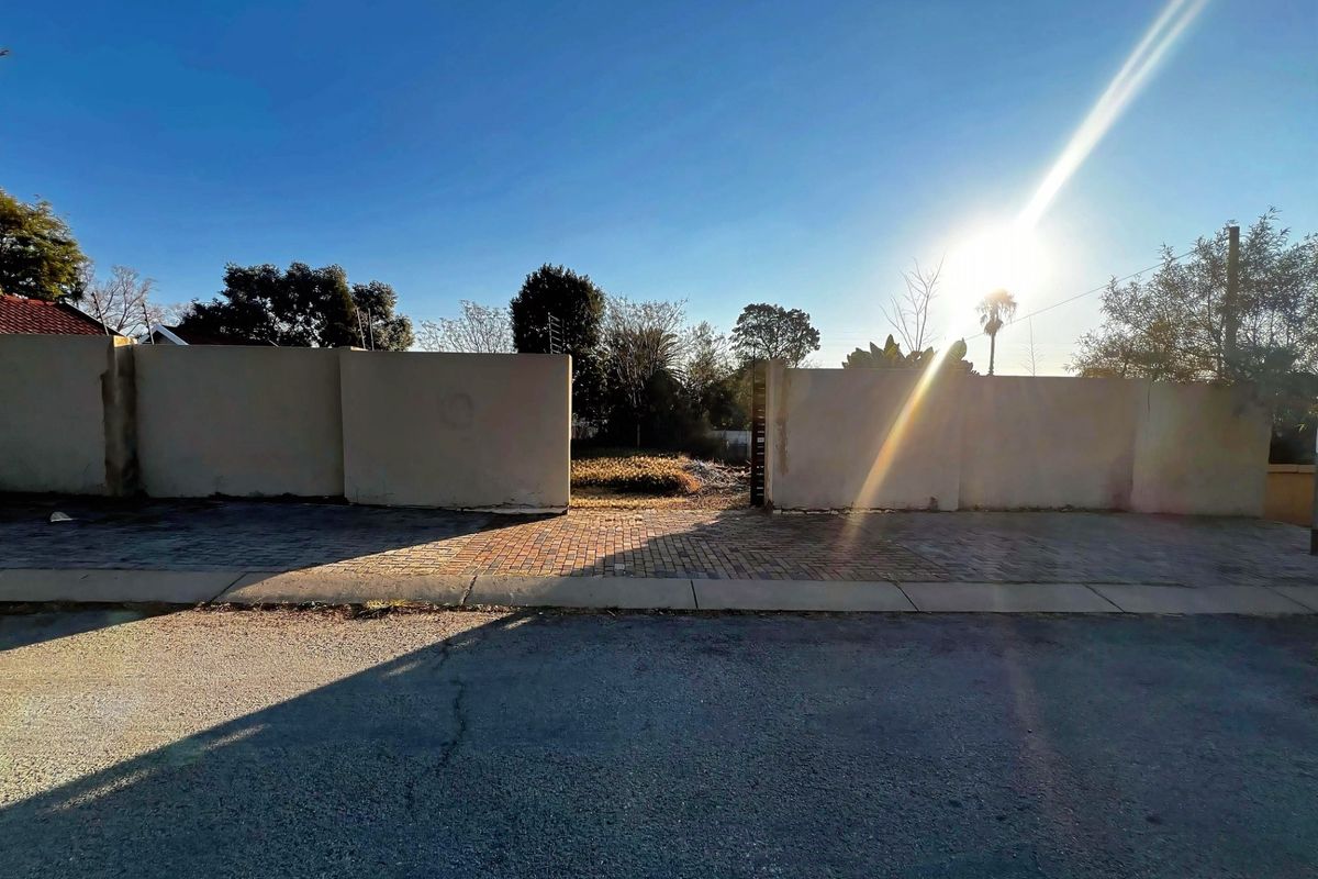 Street-level view of a vacant residential plot featuring a paved driveway entrance and perimeter boundary walls.