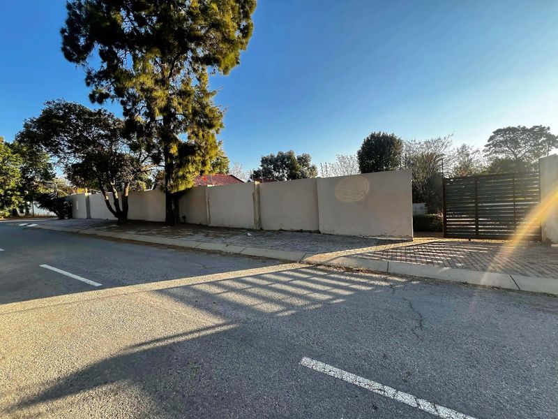 Street view of the property showing the perimeter wall, metal entrance gate, and paved driveway access.