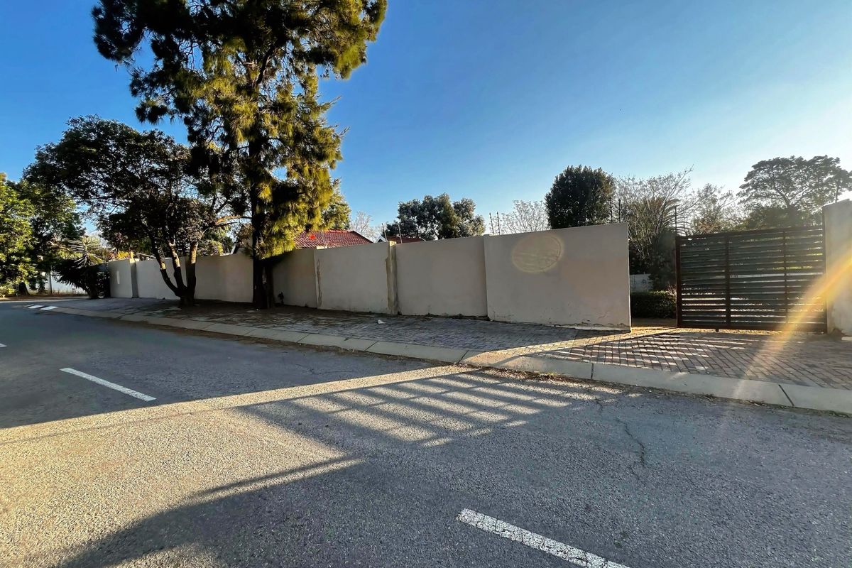 Street view of the property showing the perimeter wall, metal entrance gate, and paved driveway access.