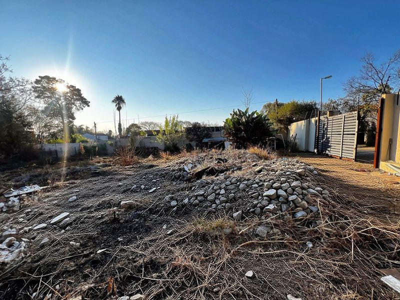 A vacant residential plot featuring a perimeter wall with electric fencing and a metal gate, currently containing a pile of rubble and debris.