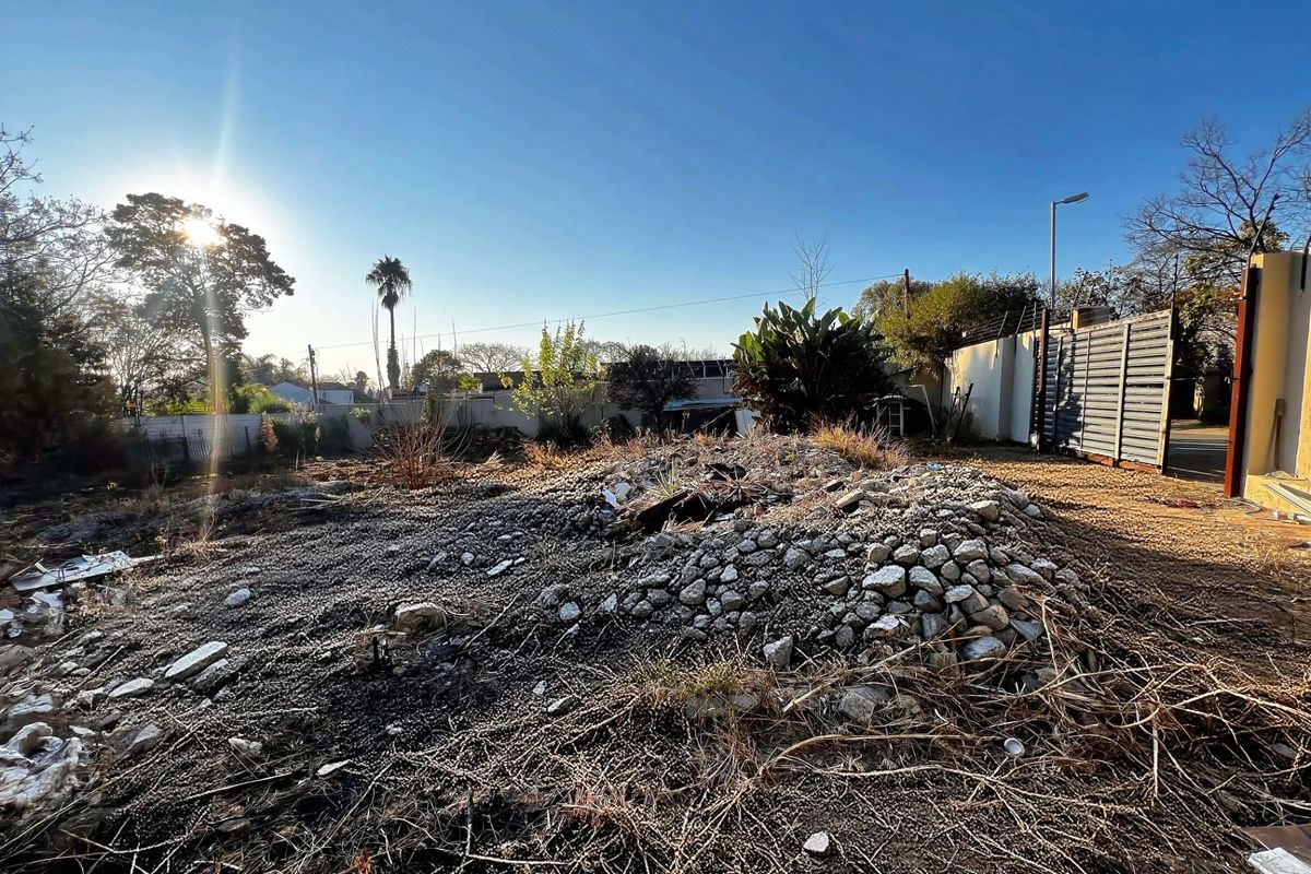 A vacant residential plot featuring a perimeter wall with electric fencing and a metal gate, currently containing a pile of rubble and debris.