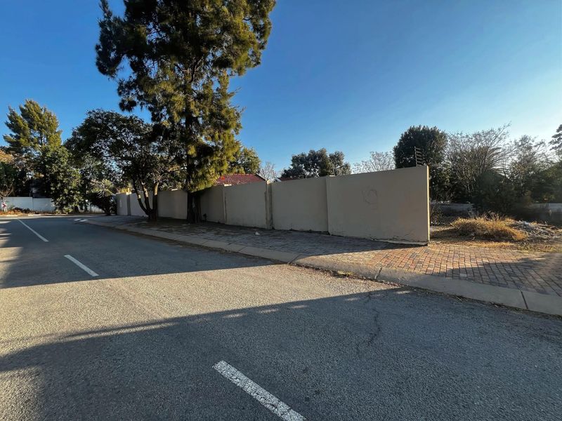 Street view of the property showing the paved sidewalk and the perimeter wall with integrated electric fencing.