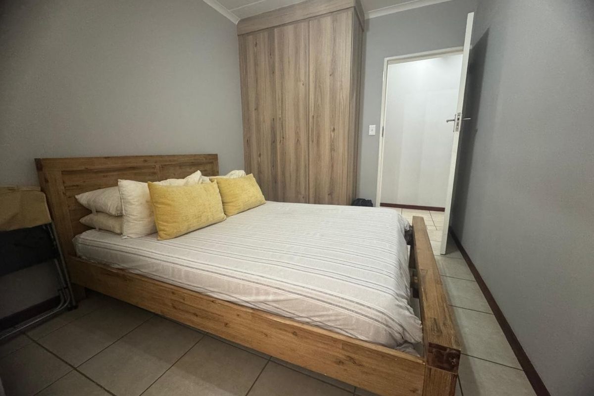 A bedroom featuring neutral grey walls, tiled flooring, and a built-in wooden wardrobe.