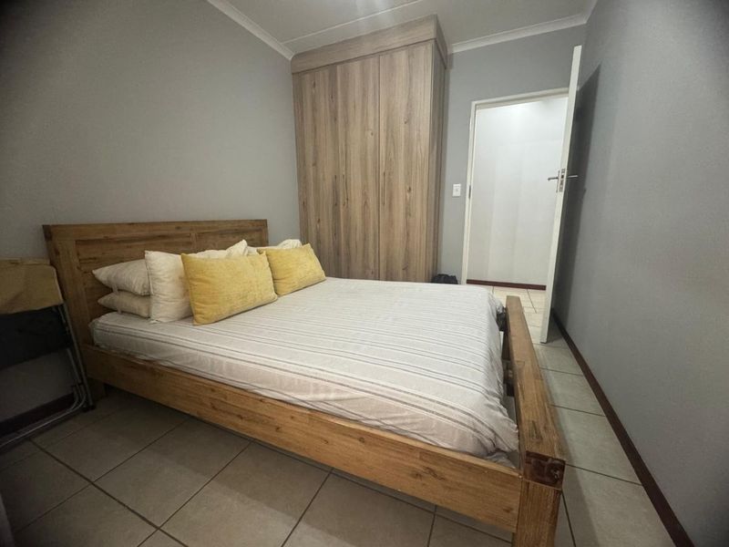 A bedroom featuring neutral grey walls, tiled flooring, and a built-in wooden wardrobe.