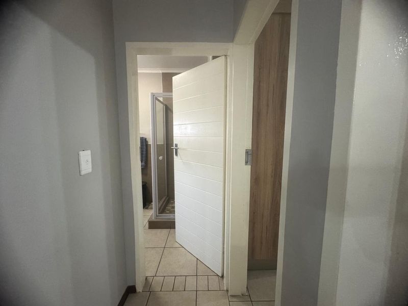 A clean hallway featuring tiled flooring and access to a bathroom and built-in storage cupboard.