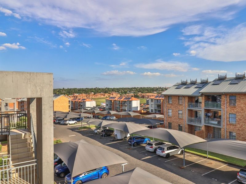 Elevated view overlooking the apartment complex parking area featuring shade cloth carports and surrounding residential buildings under a clear blue sky.