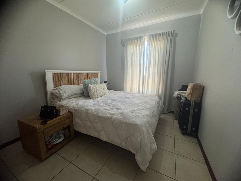 A functional bedroom featuring neutral wall tones, tiled flooring, and window treatments, providing a clean and simple living space.