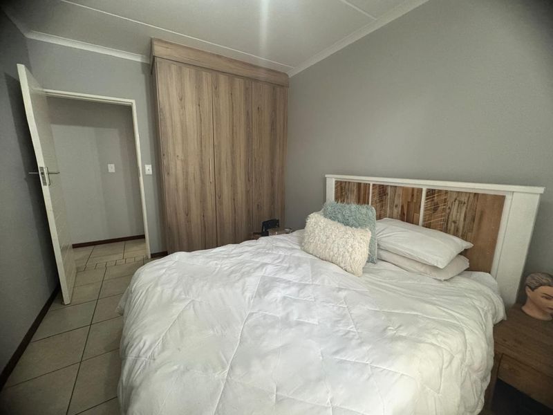 A well-maintained bedroom featuring neutral wall tones, tiled flooring, and a large built-in wooden wardrobe providing ample storage space.