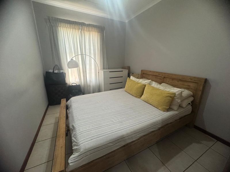 A functional bedroom featuring tiled flooring, neutral wall finishes, and window treatments, providing a comfortable and well-lit sleeping space.