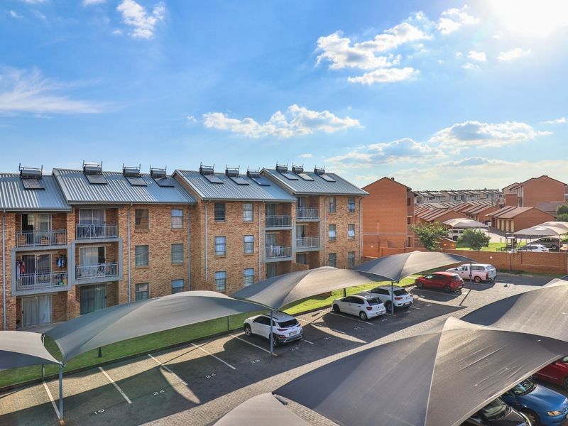 Aerial view of an apartment complex featuring brick facades, metal roofing with solar water heaters, private balconies, and covered parking bays.