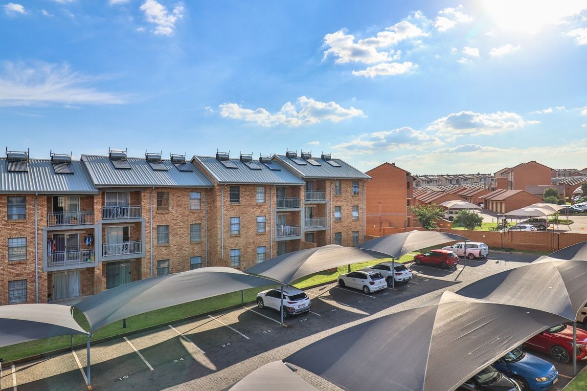 Aerial view of an apartment complex featuring brick facades, metal roofing with solar water heaters, private balconies, and covered parking bays.