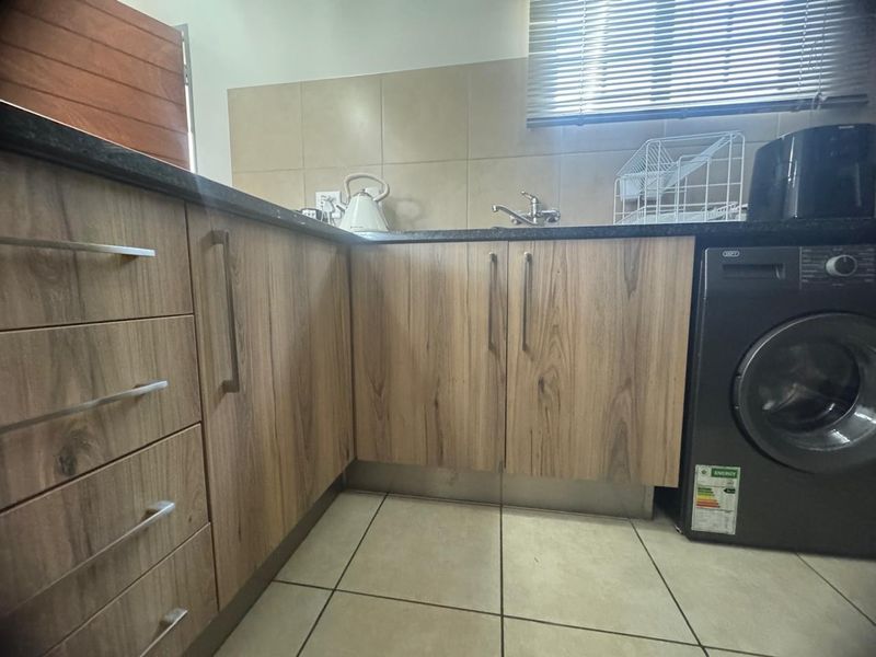 A functional kitchen featuring wood-look laminate cabinetry, granite countertops, a stainless steel sink, and neutral tiled flooring with a tiled backsplash.