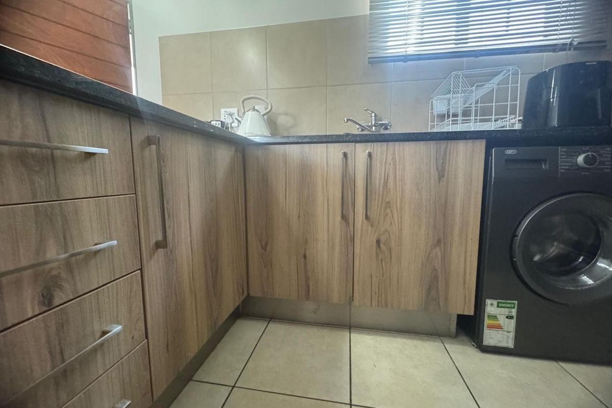 A functional kitchen featuring wood-look laminate cabinetry, granite countertops, a stainless steel sink, and neutral tiled flooring with a tiled backsplash.