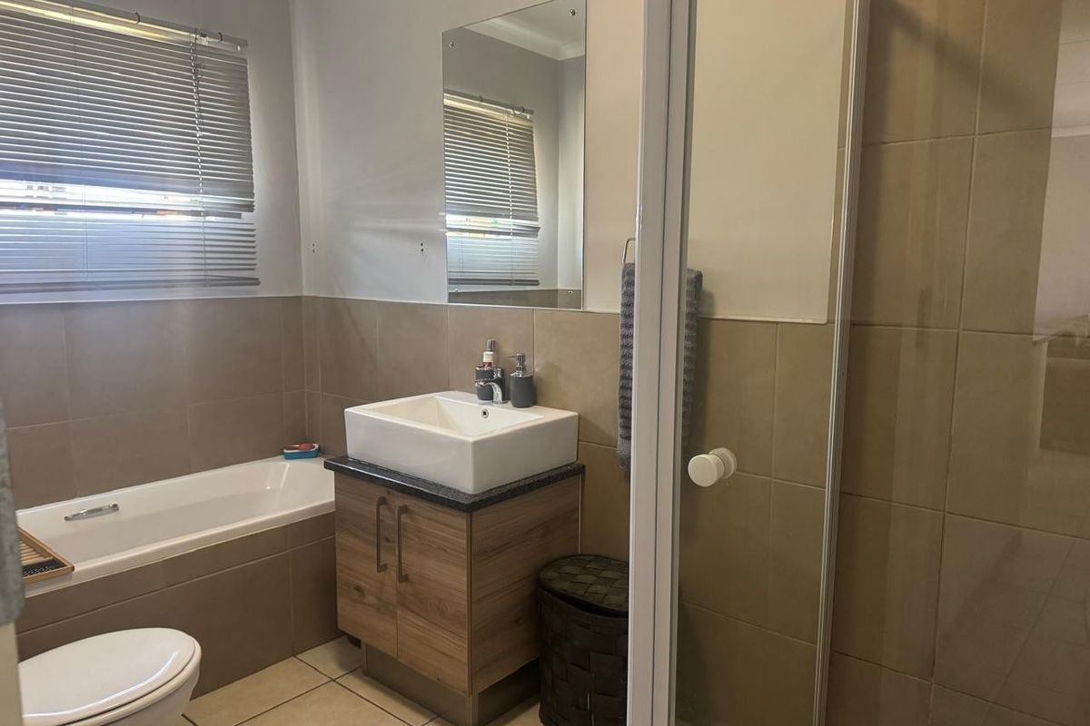 A well-maintained bathroom featuring a bathtub, separate shower enclosure, modern vessel sink vanity, and neutral wall and floor tiling.
