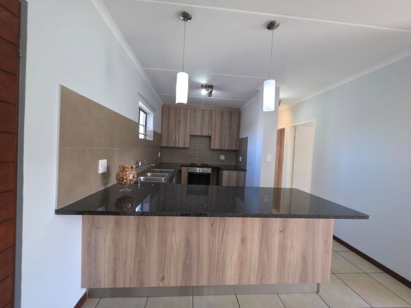 Modern kitchen featuring wood-look cabinetry, granite countertops, a built-in oven, and a breakfast bar, finished with neutral wall tones and tiled flooring.