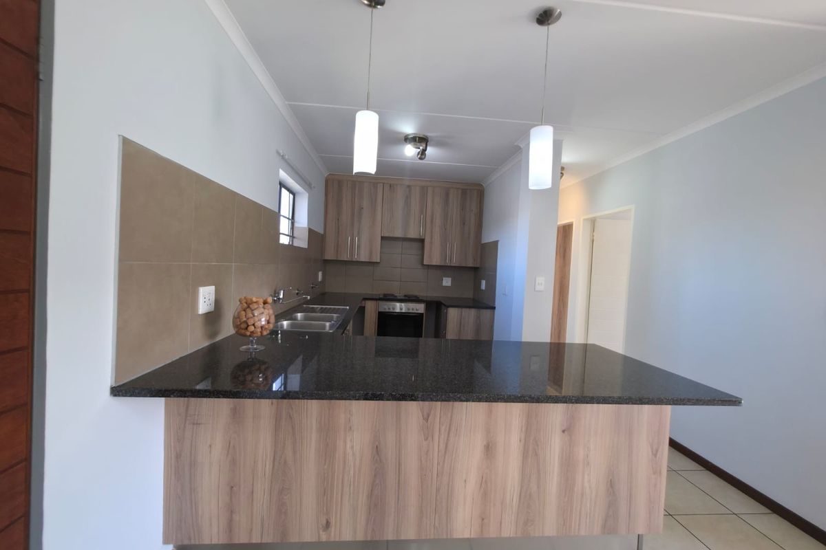 Modern kitchen featuring wood-look cabinetry, granite countertops, a built-in oven, and a breakfast bar, finished with neutral wall tones and tiled flooring.