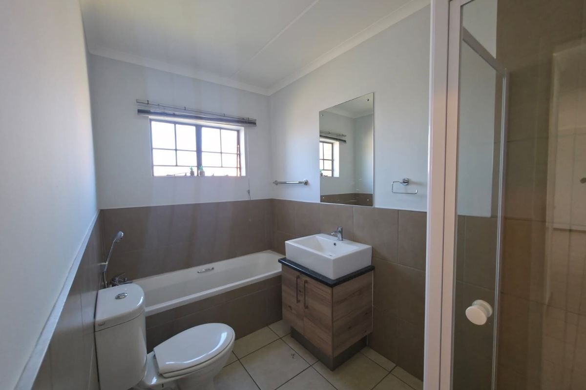 A clean, functional bathroom featuring a bathtub, separate shower enclosure, modern vanity with basin, and neutral wall tiling.