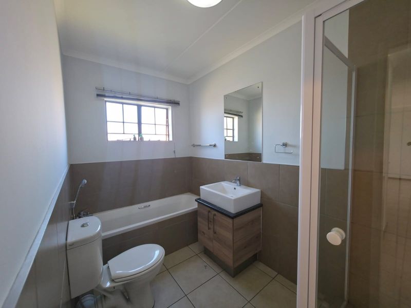 A clean, functional bathroom featuring a bathtub, separate shower enclosure, modern vanity with basin, and neutral wall tiling.