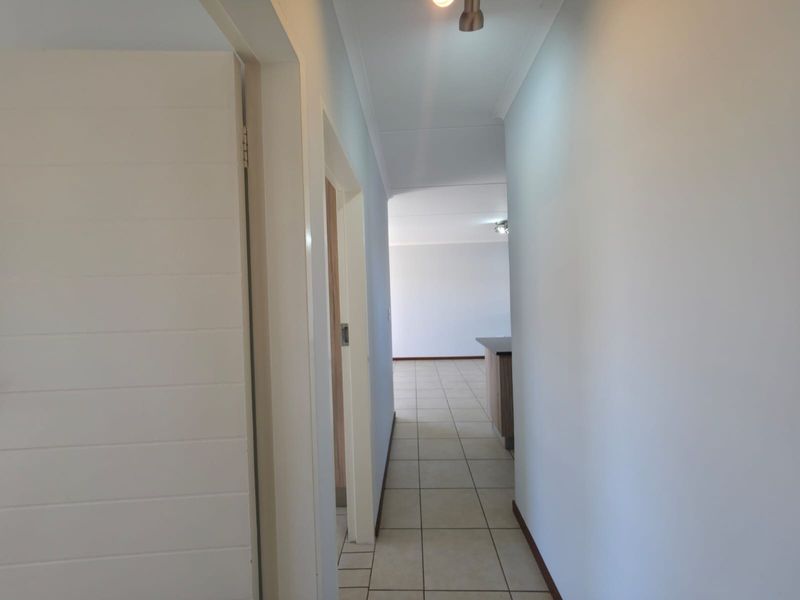 A clean, neutral hallway with tiled flooring leading towards an open-plan living area.