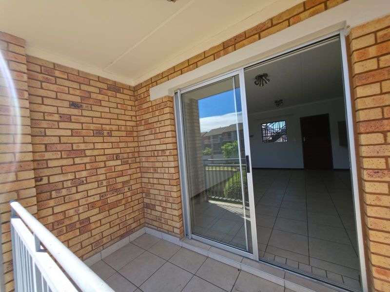 A clean, covered balcony featuring exposed brick walls, tiled flooring, and a sliding glass door providing access to the interior living space.