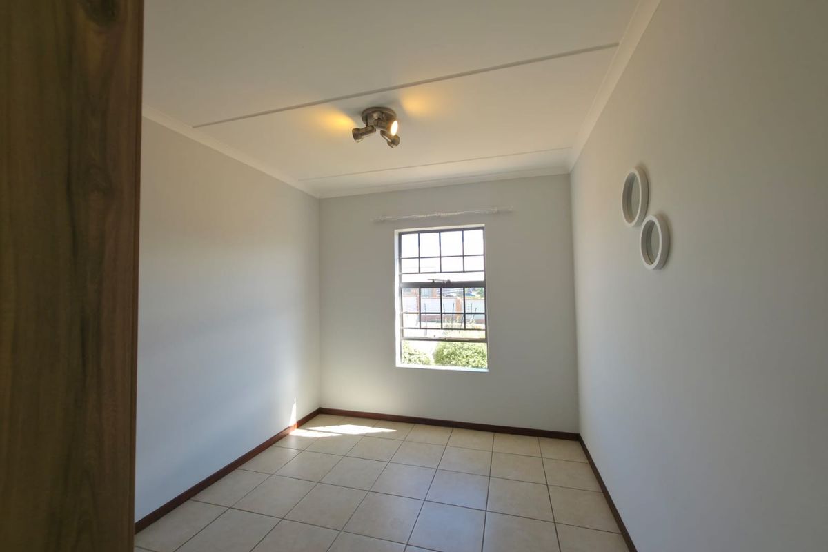A bright, empty bedroom featuring neutral tiled flooring, a window with security bars, and a modern ceiling-mounted spotlight fixture.