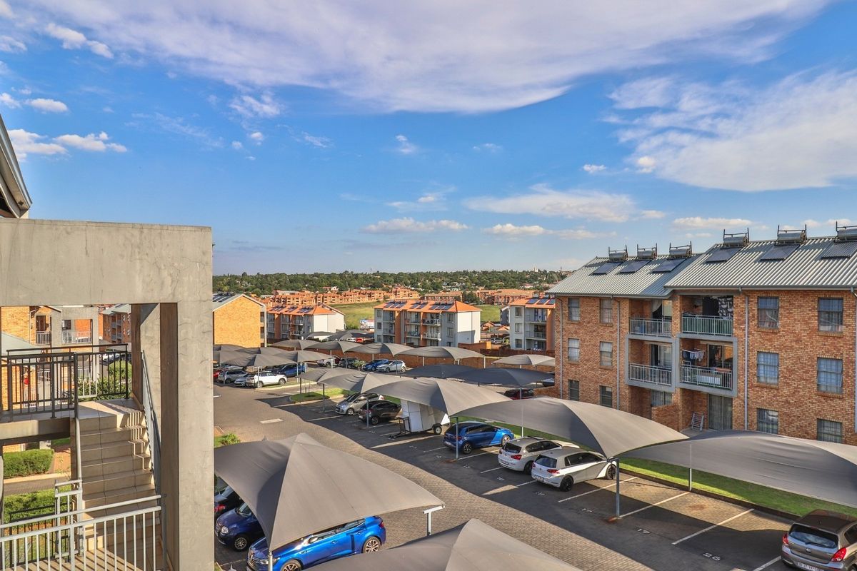 An elevated view of an apartment complex featuring brick buildings, paved parking areas with shade cloth carports, and solar water heating systems.