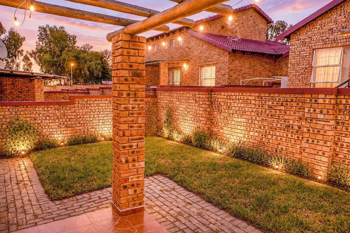 A well-maintained rear garden featuring a brick boundary wall, paved patio area, and a timber pergola with integrated outdoor lighting.