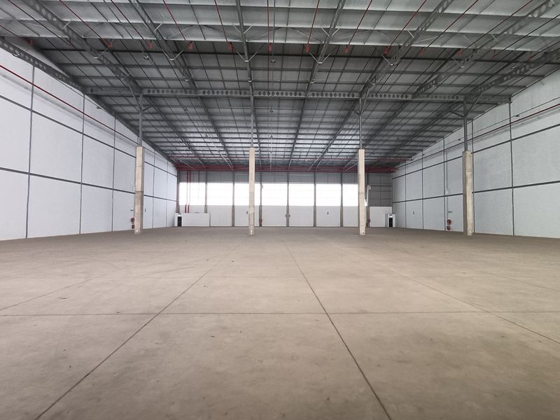 Spacious industrial warehouse unit featuring high ceilings, exposed steel trusses, concrete flooring, and integrated fire sprinkler systems, suitable for storage or manufacturing operations.