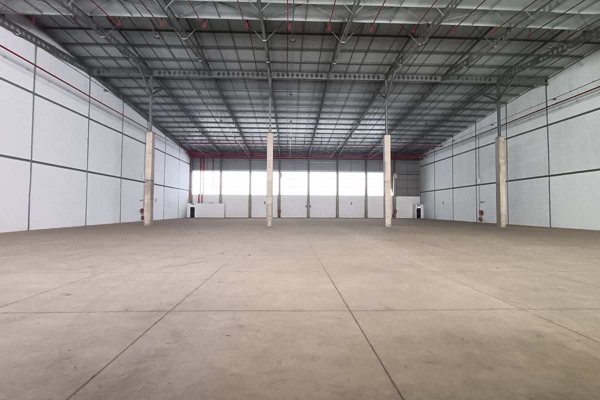 Spacious industrial warehouse unit featuring high ceilings, exposed steel trusses, concrete flooring, and integrated fire sprinkler systems, suitable for storage or manufacturing operations.