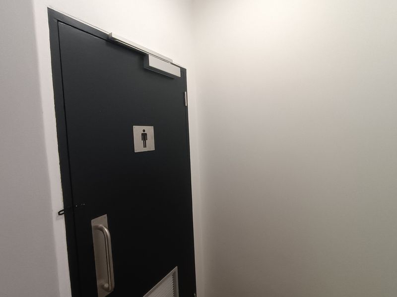 A clean, minimalist hallway featuring a black commercial-style door with a pull handle and integrated ventilation grille.