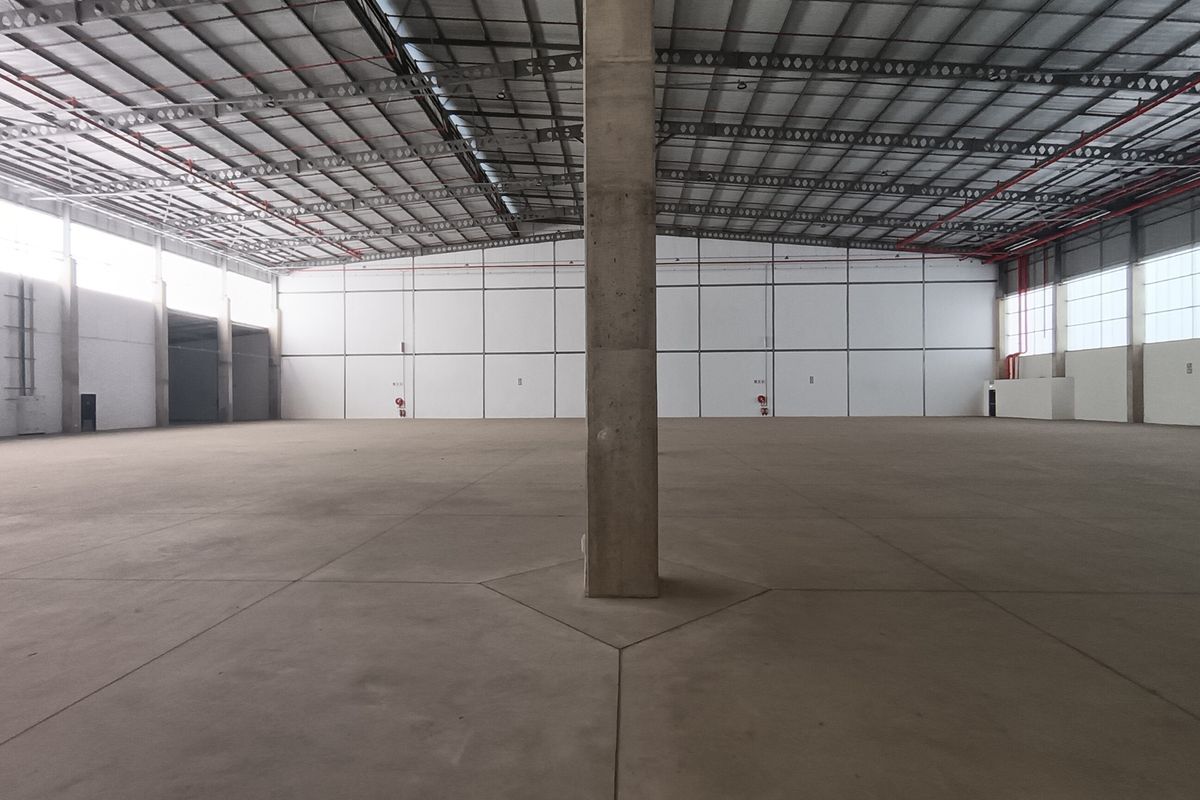 A spacious, empty industrial warehouse featuring high ceilings with exposed steel trusses, polished concrete flooring, and large windows providing ample natural light.