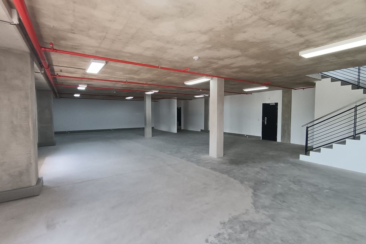A spacious, open-plan industrial utility area featuring exposed concrete ceilings, fire sprinkler systems, and a staircase with metal railings.