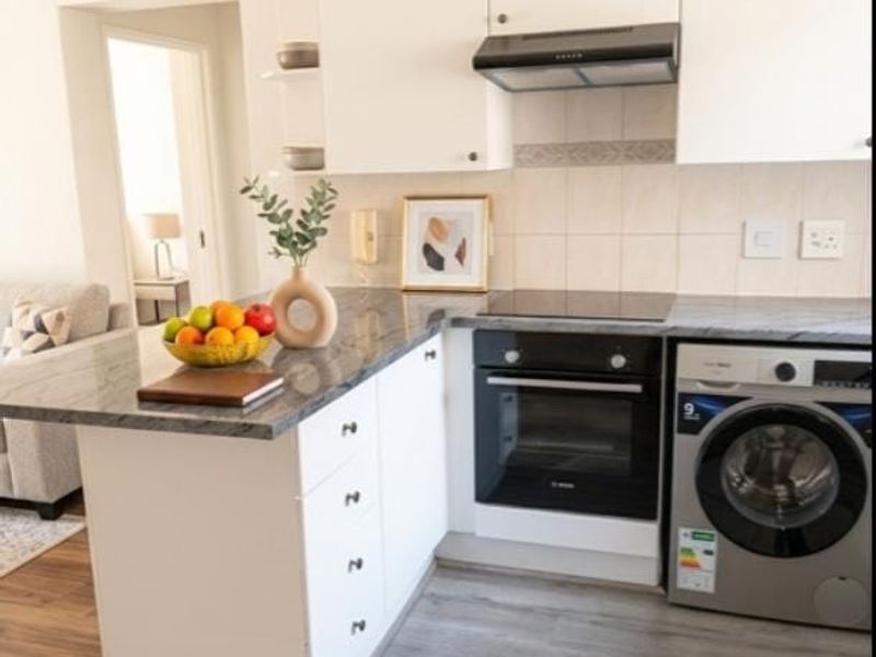 Modern kitchen featuring white cabinetry, granite countertops, built-in oven, electric hob, extractor fan, and integrated laundry appliance with durable laminate flooring.