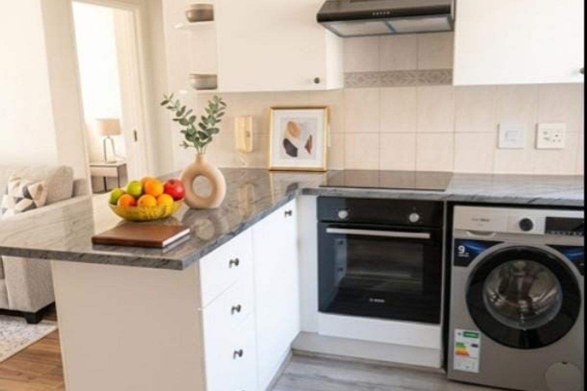 Modern kitchen featuring white cabinetry, granite countertops, built-in oven, electric hob, extractor fan, and integrated laundry appliance with durable laminate flooring.
