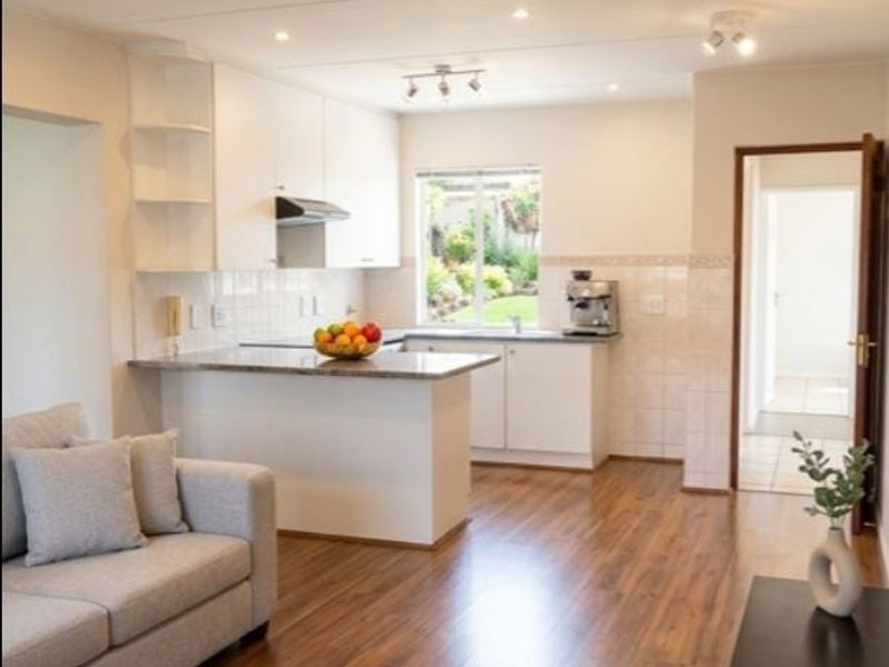 Bright open-plan living and kitchen area featuring modern laminate flooring, sleek white cabinetry, granite countertops, and integrated lighting throughout.