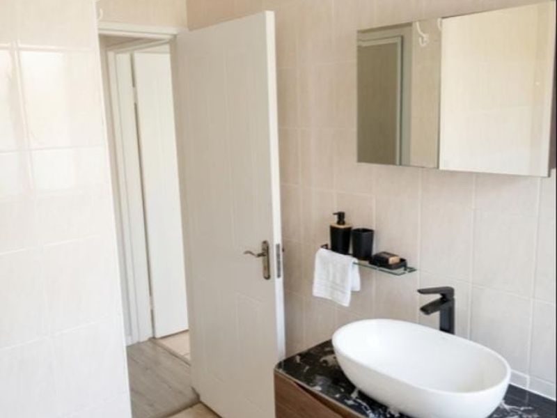 A modern bathroom featuring a stylish vessel sink with a black faucet, marble-topped vanity cabinet, and wall-mounted mirror cabinet with neutral tiled finishes.