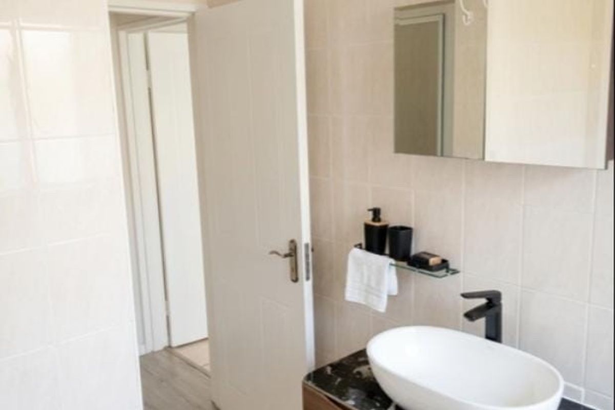 A modern bathroom featuring a stylish vessel sink with a black faucet, marble-topped vanity cabinet, and wall-mounted mirror cabinet with neutral tiled finishes.