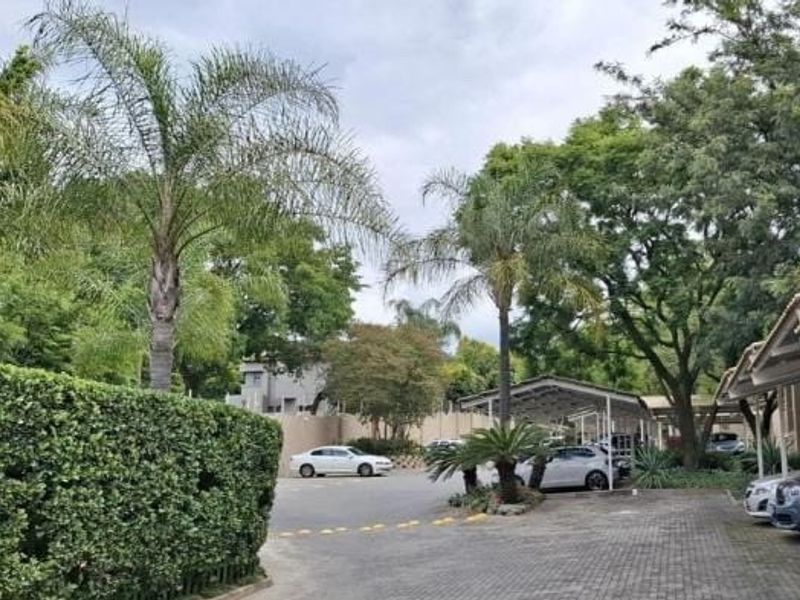 Exterior view of the apartment complex featuring paved parking areas, covered carports, and established garden landscaping.