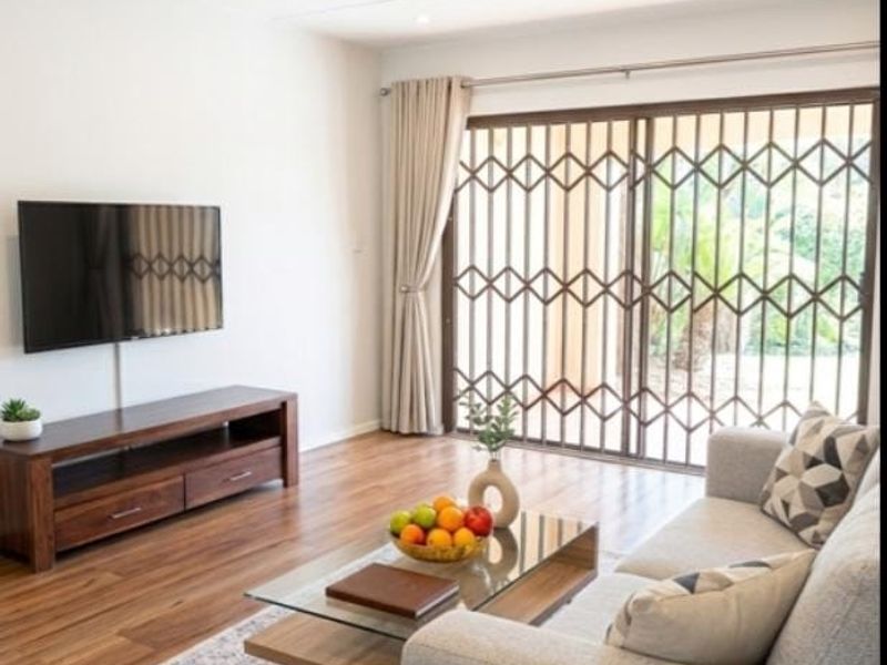 A bright living room featuring laminate flooring, recessed downlights, and a sliding glass door with a security gate leading to the outdoors.