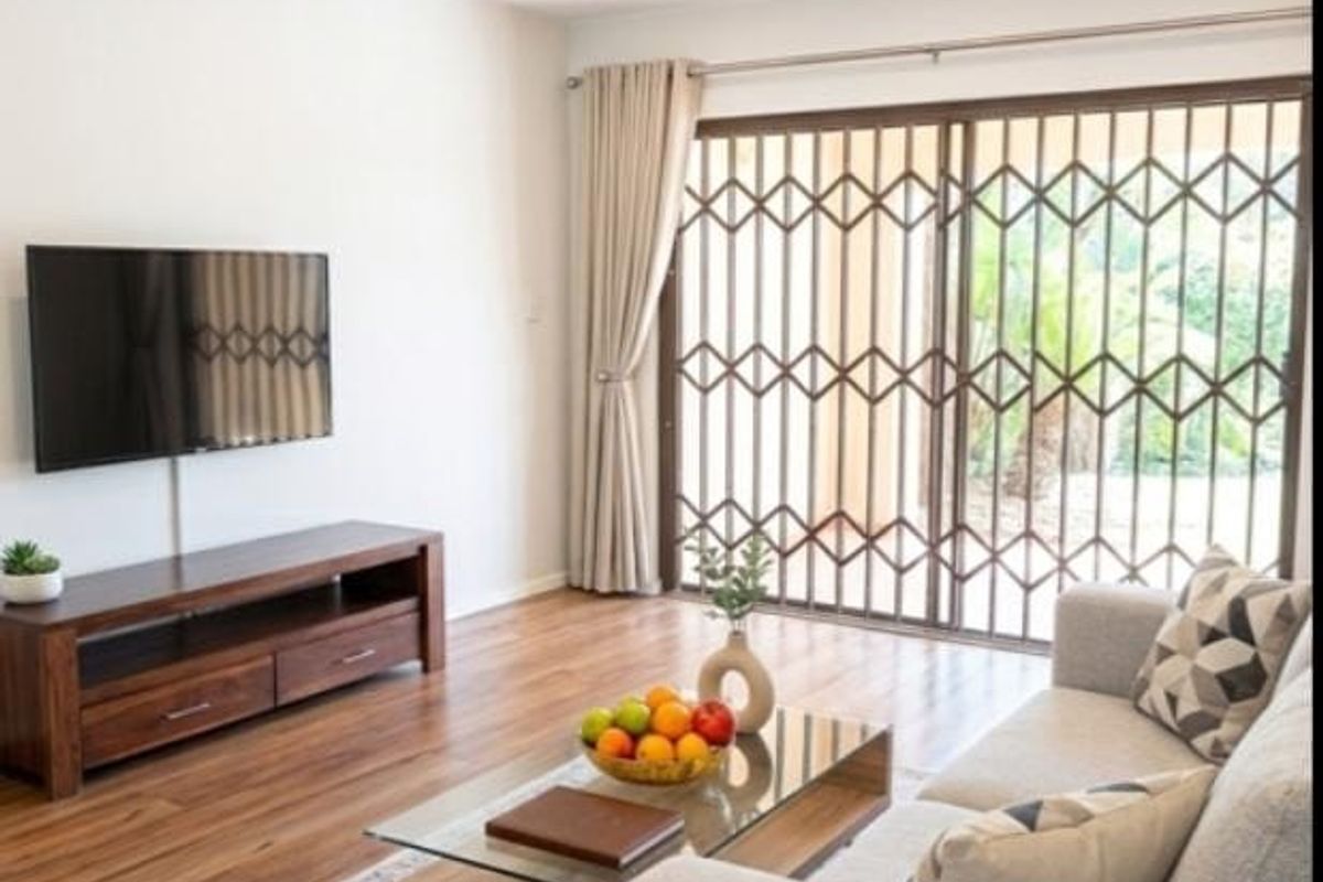 A bright living room featuring laminate flooring, recessed downlights, and a sliding glass door with a security gate leading to the outdoors.