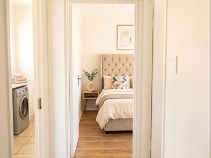 A bright hallway featuring laminate flooring, providing access to a bedroom and a laundry area.