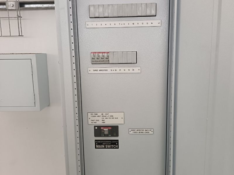 A clean, well-maintained industrial electrical distribution board for Unit 2 Warehouse 2, featuring clearly labeled circuit breakers and surge protection equipment.