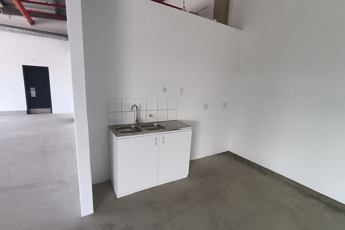 A compact industrial kitchenette featuring a stainless steel sink, base cabinetry, and tiled splashback within an open-plan warehouse space.